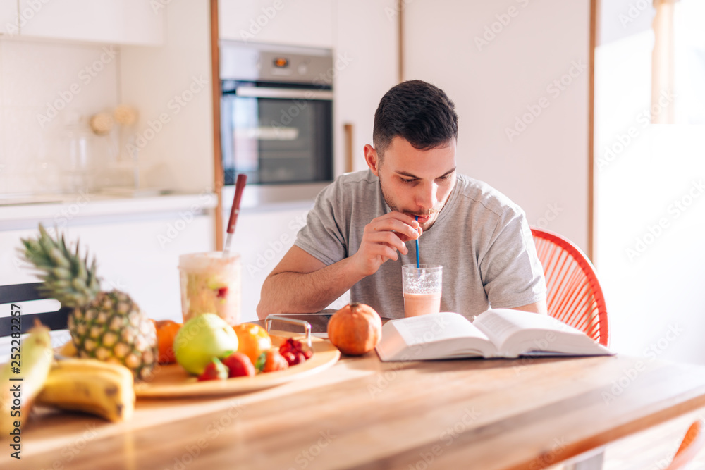 healthy strong young man reading a book early in the morning while making his smoothie. healthy strong young man reading a book early in the morning while making his smoothie.