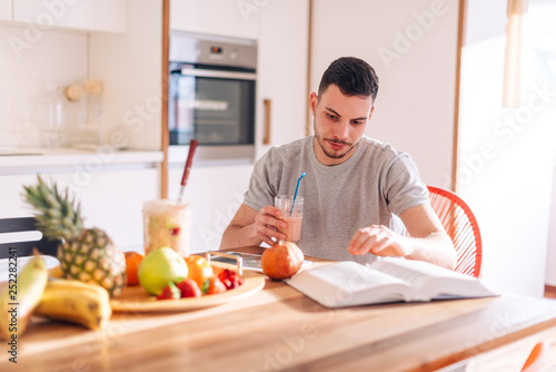 healthy strong young man reading a book early in the morning while making his smoothie.