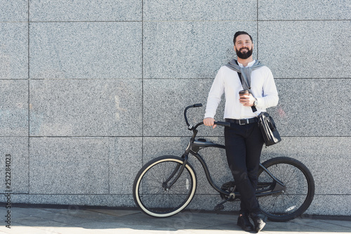 Young businessman holding cup of coffee while leaning at his bicycle