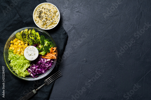 Salad bowl, healthy and balanced food. Ingredients broccoli, corn, carrots, couscous, lettuce, cabbage, sauce. Black background, top view, space for text