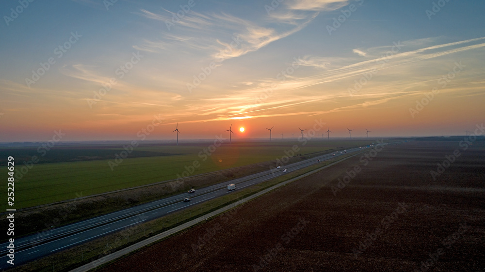Fototapeta premium Wind turbines along the highway at sunset, France