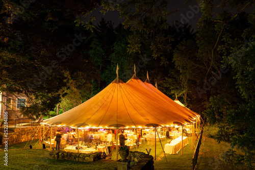 a wedding tent at night surrounded by trees with an orange glow from the lights, long exposure - wedding tent series