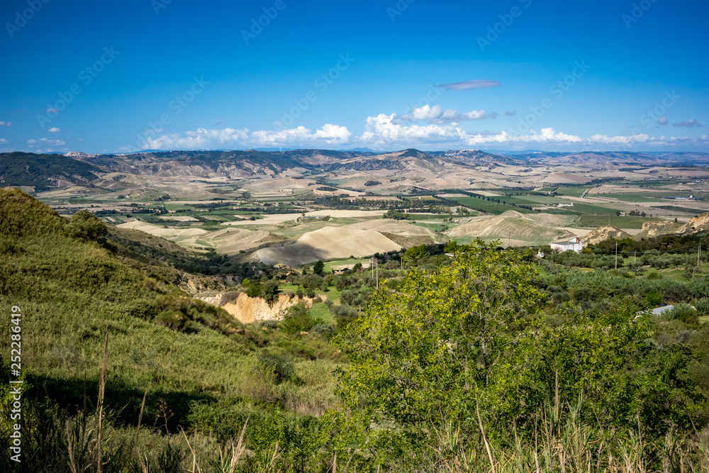 Valley countryside landscape, Basilicata, Italy, sunny summer day, green hills and clear blue sky, blurred wind power turbines far away in the background