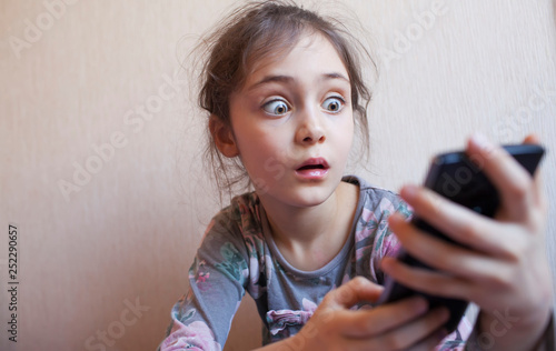 Little girl looks on a smartphone display with surprise and fright photo