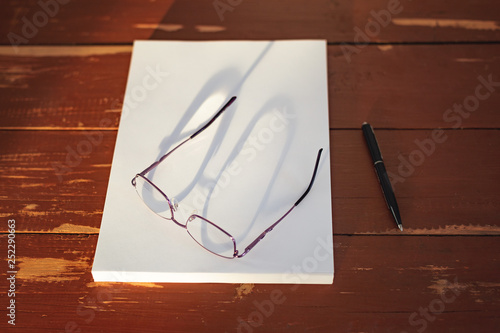 A stack of blank sheets of paper, a pen and glasses on a Red wooden table