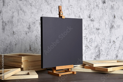 Black blank cotton canvas for acrylic and oil paints, a wooden easel and stretcher bars on table