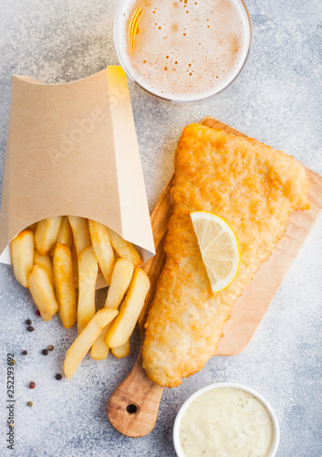 Fototapeta Naklejka Na Ścianę i Meble -  Traditional British Fish and Chips with tartar sauce abd glass of craft lager beer on chopping board on white stone table background. Top view