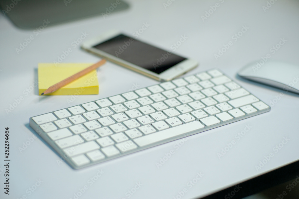 Selective focus on white keyborad on the desk with defocused stationary, mouse, and mobile phone in background Selective focus on white keyborad on the desk with defocused stationary, mouse, and mobile phone in background