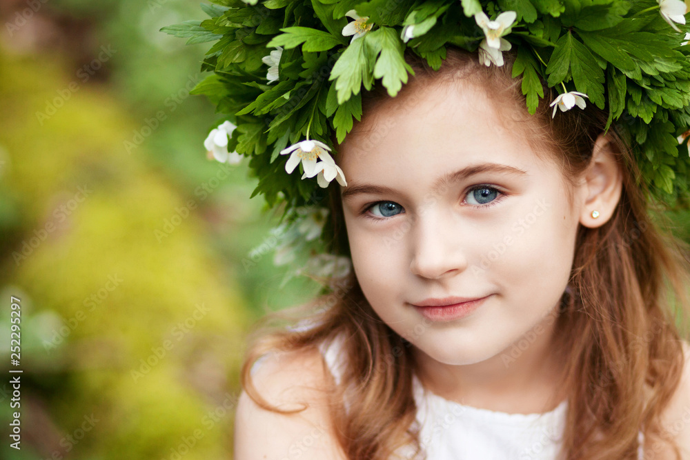 Beautiful little girl in a white dress in the spring wood. Portrait of the pretty little girl with a wreath from spring flowers on the head. Easter time Beautiful little girl in a white dress in the spring wood. Portrait of the pretty little girl with a wreath from spring flowers on the head. Easter time