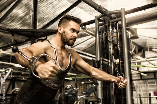 Handsome young muscular athlete doing chest workout on cable crossover machine