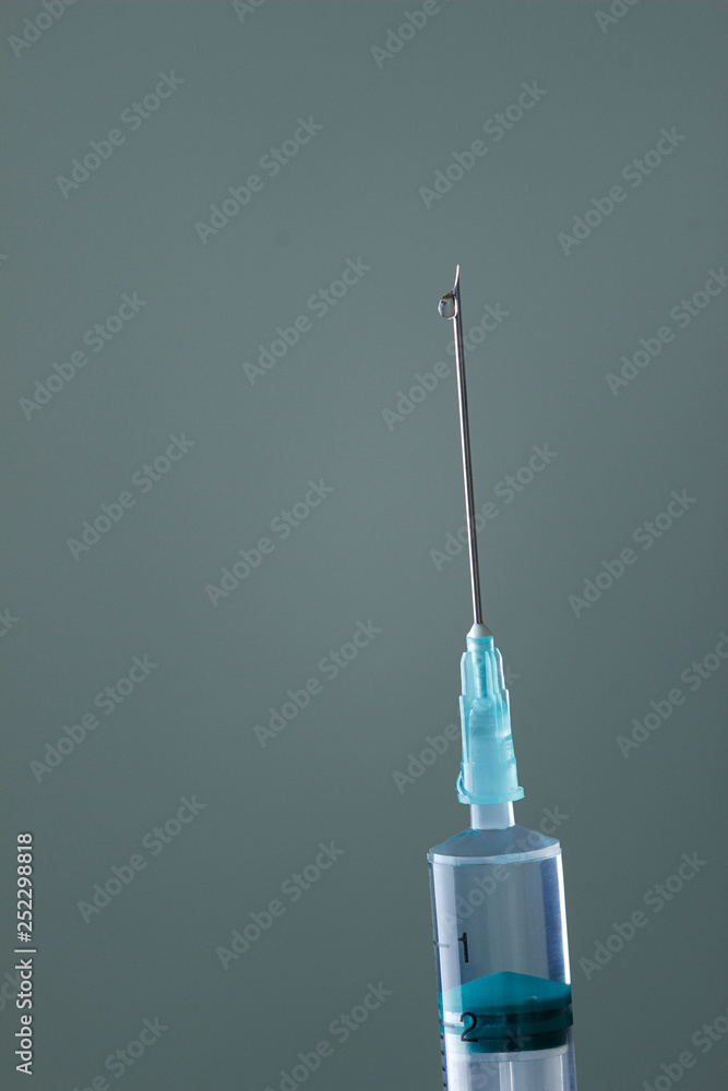 The end of the syringe with a needle filled with liquid, on a neutral background. The end of the syringe with a needle filled with liquid, on a neutral background.