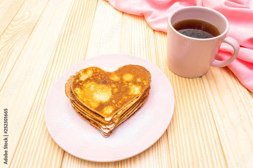 Heart shaped pancakes for romantic breakfast with strawberry jam and black tea. Shrovetide (carnival) concept. On wooden background