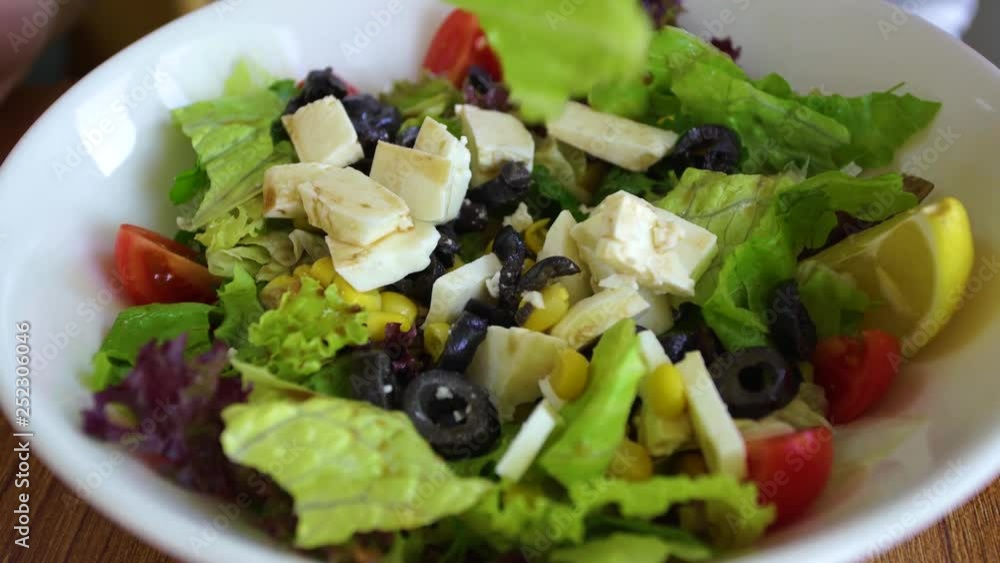 Person eating healthy salad. Closeup view of white plate full of salad, fork and knife in hands of man. Real time 4k video footage.