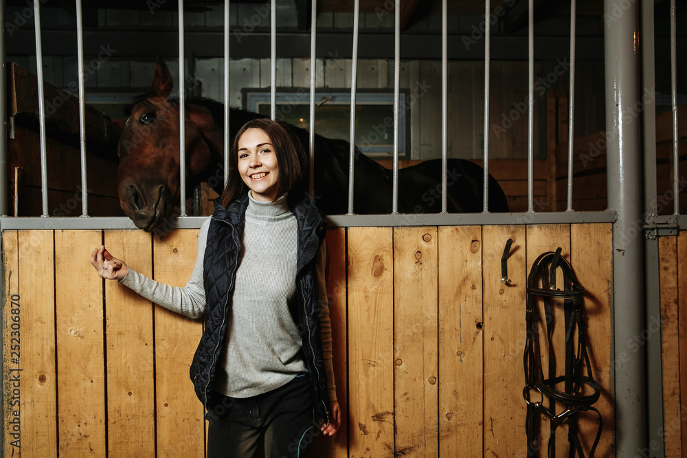 Portrait of smiling female jockey standing by horse in stable Portrait of smiling female jockey standing by horse in stable