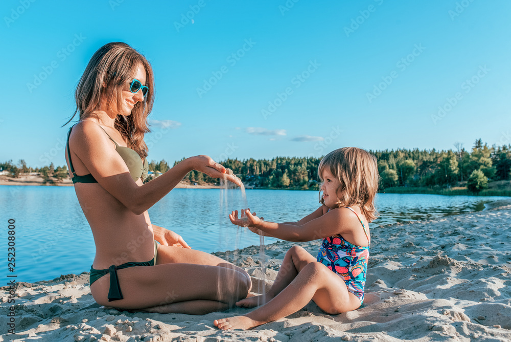 custom made wallpaper toronto digitalA young mother plays with her daughter for 2-5 years, in the summer on the beach in sand, near water against the background of forest. Happy relaxing at the resort, happy family outdoor recreation.