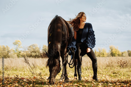 pretty woman with black horse in autumnal nature. Fashion photoshoot