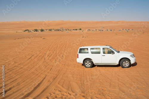 Off-road vehicle in the Wahiba Sand Desert and Bedouin camp in the background (Oman)