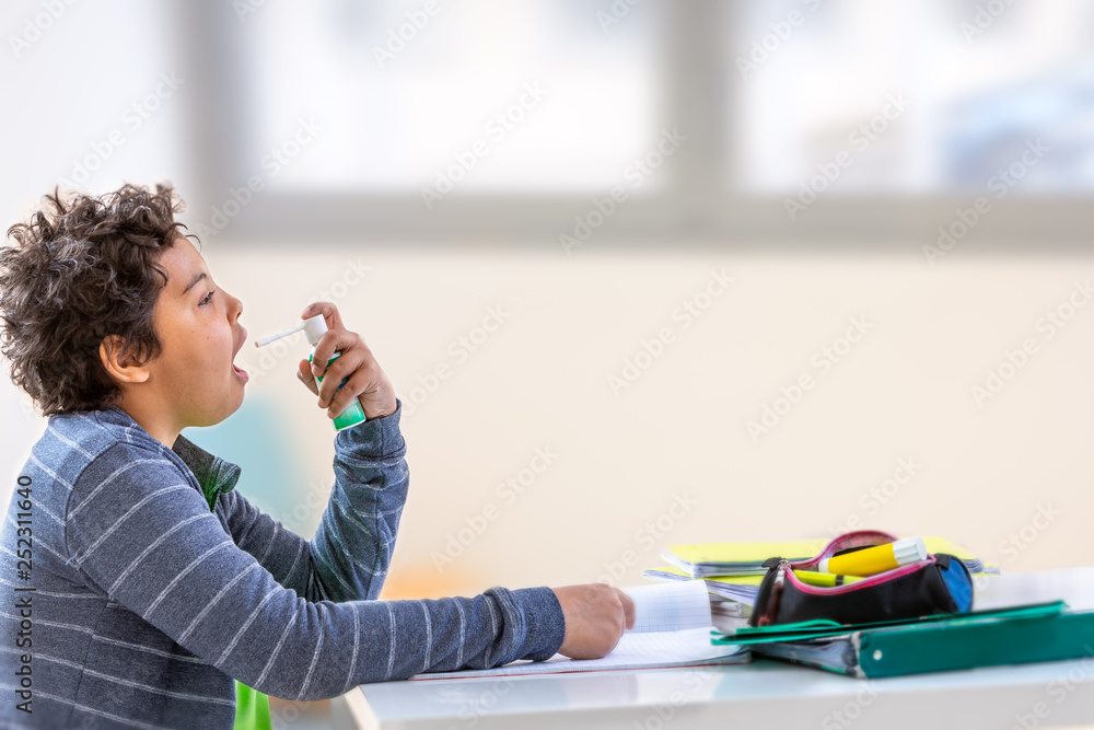 Boy splashes in his mouth with a spray from the pain in her throat while doing homework