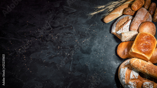 Assortment of fresh baked bread on dark background. White and rye bread, buns with copy place