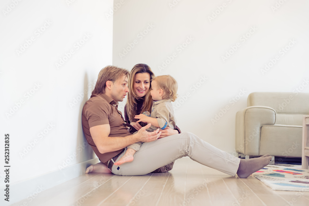 Happy family sitting on floor with their little baby. Family spending time at home with their son.
