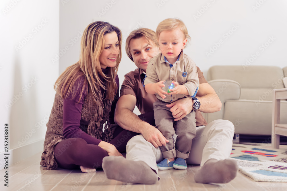 Happy family sitting on floor with their little baby. Family spending time at home with their son.