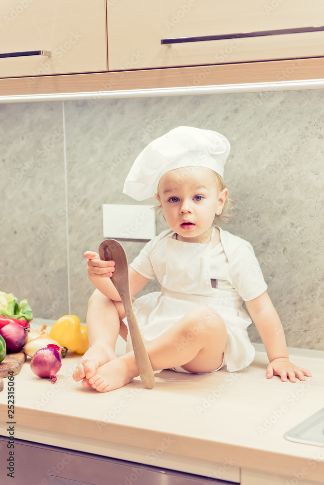Baby boy sitting among vegetables in the kitchen and prepares for cooking Baby boy sitting among vegetables in the kitchen and prepares for cooking