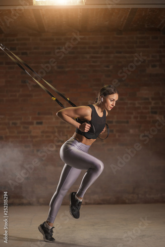 Sportive caucasian women training arms with trx fitness straps in the gym doing Sprinter Start exercise, muscles of upper body chest shoulders pecs and triceps.