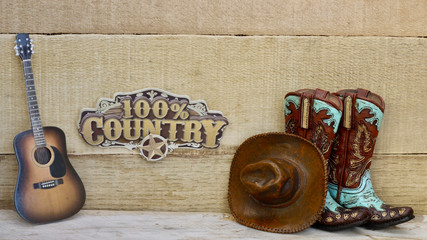 Cowboy boots, hat,guitar with 100% country banner on a wood background with writing space