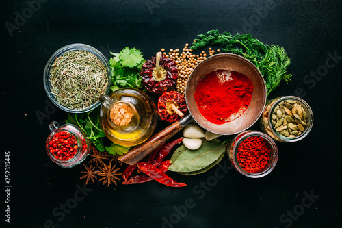 From above set of various spices and herbs placed on black background around bottle of oil photo