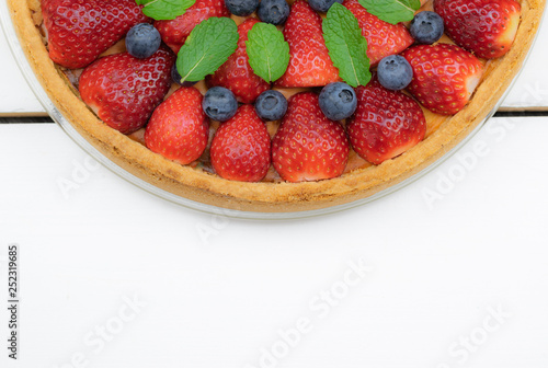  Homemade tart with strawberries and blueberries on a background from white boards.