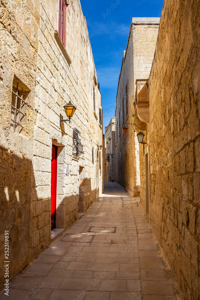 Sunny midday beautiful narrow typical limestone street with lanterns in Mdina - Citta Vecchia or Citta Notabile in Malta