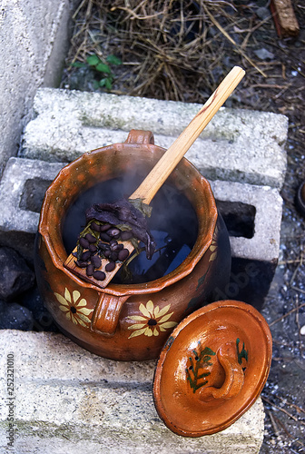  clay pot on outdoor brick fire pit, with wooden spoon and black beans, top view