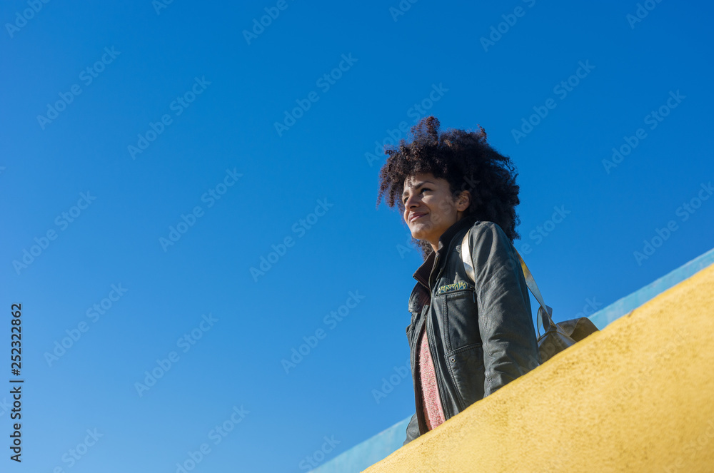 Black woman with afro hair leaning against brightly colored walls while looking at her smartphone and having a coffee Black woman with afro hair leaning against brightly colored walls while looking at her smartphone and having a coffee