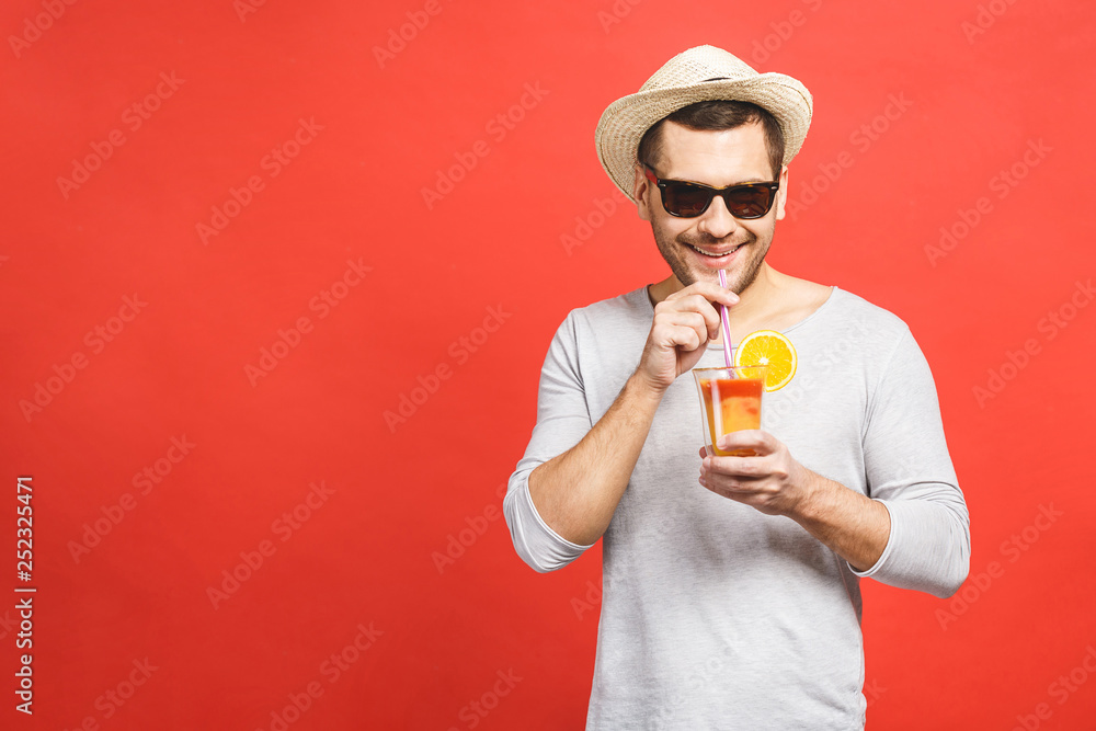 Portrait of attractive young man in hat and sunglasses standing and drinking orange juice over red background. Portrait of attractive young man in hat and sunglasses standing and drinking orange juice over red background.
