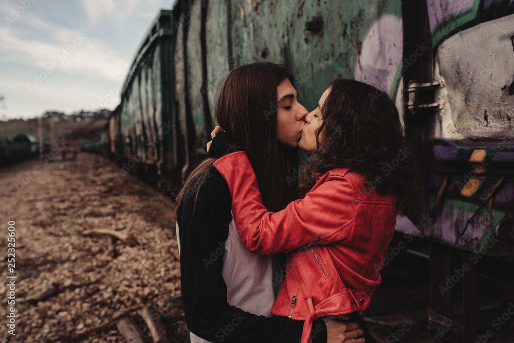 Side view of young hipsters embracing and kissing near old locomotive on railroad Side view of young hipsters embracing and kissing near old locomotive on railroad