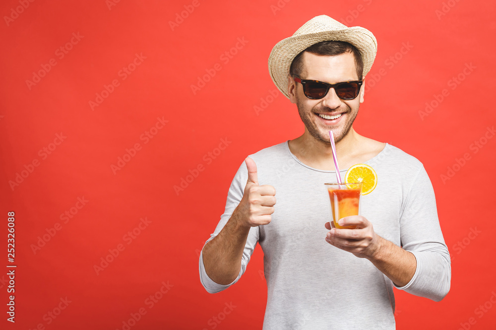 Portrait of attractive young man in hat and sunglasses standing and drinking orange juice over red background. Thumbs up. Portrait of attractive young man in hat and sunglasses standing and drinking orange juice over red background. Thumbs up.
