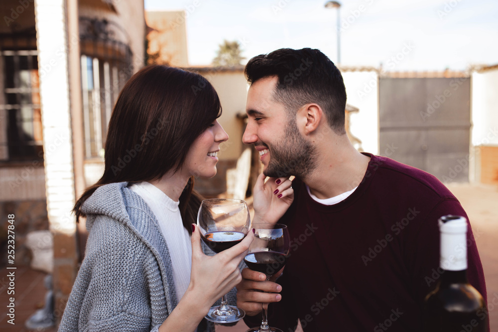 Handsome man and beautiful woman smiling and looking at each other while sitting on terrace and enjoying fine wine together Handsome man and beautiful woman smiling and looking at each other while sitting on terrace and enjoying fine wine together