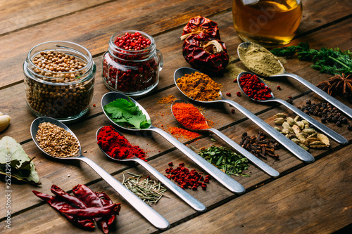 Bunch of assorted spices placed in order on lumber tabletop near bottle of oil photo