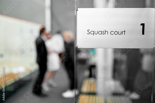 Squash court sign on the glass with a man on the background 