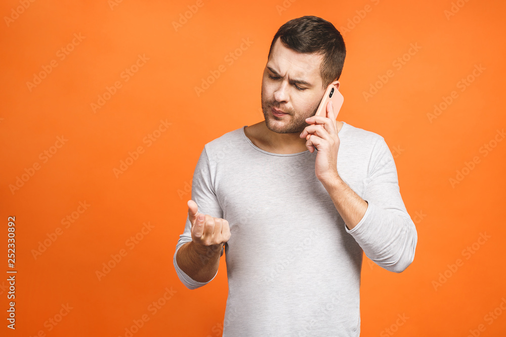 Serious young man talking on mobile isolated on orange background. Using phone. Serious young man talking on mobile isolated on orange background. Using phone.