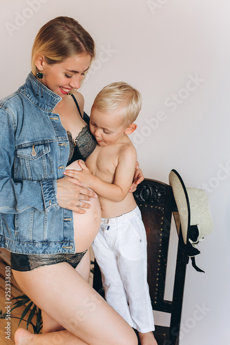 Happy pregnant expacting for a baby mother laughing ang hugging with cheerful caucasian baby boy son at home indoors together . Pregnancy, maternity, infant baby, family, childhood concept photo