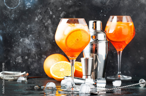 Aperol spritz cocktail in big wine glass, summer Italian low alcohol cold drink, dark bar counter background with tools, summer mood concept, selective focus