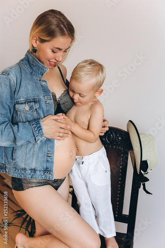 Happy pregnant expacting for a baby mother laughing ang hugging with cheerful caucasian baby boy son at home indoors together . Pregnancy, maternity, infant baby, family, childhood concept photo