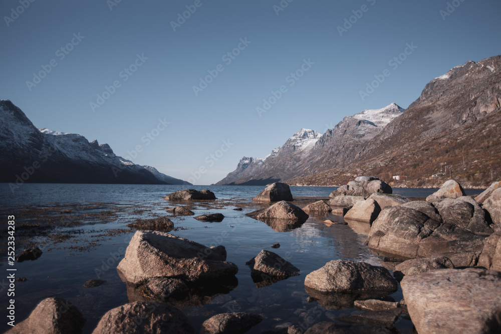 Fjord in Norway near Tromso in autumn. Deep camera position with stones in the foreground. Calm sunny weather.
