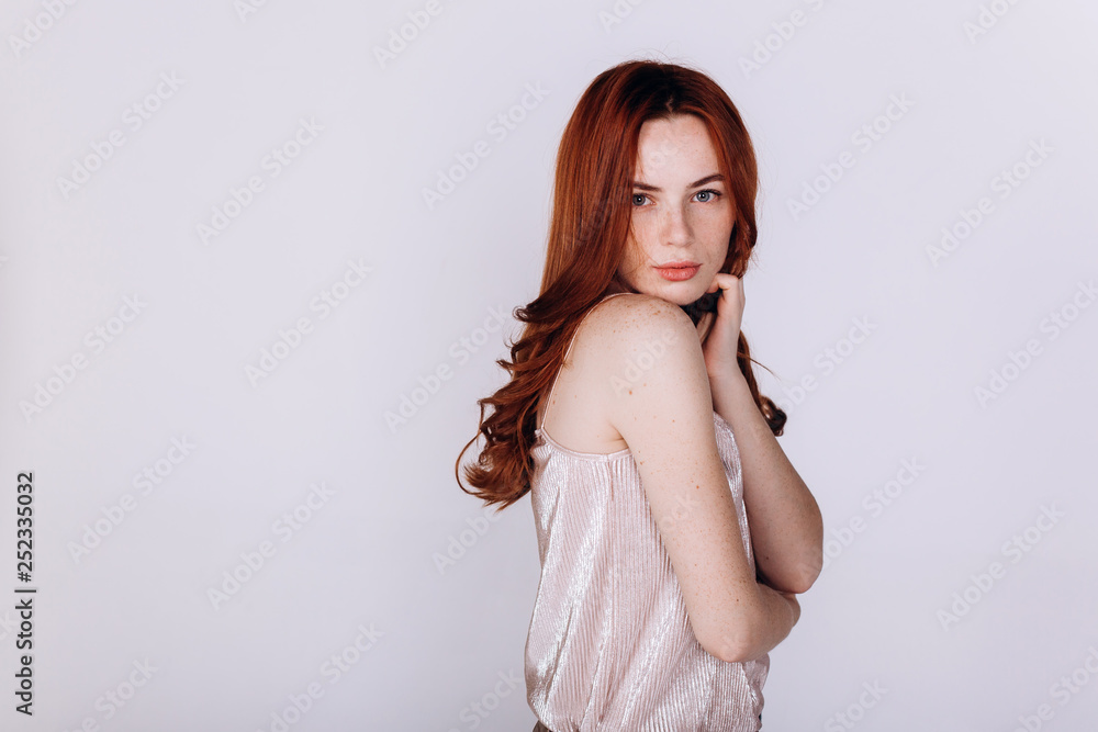 Fototapeta premium Close up portrait of young ginger pretty emotional caucasian girl with freckles posing in studio on grey background. Beauty, casual, fashion concept