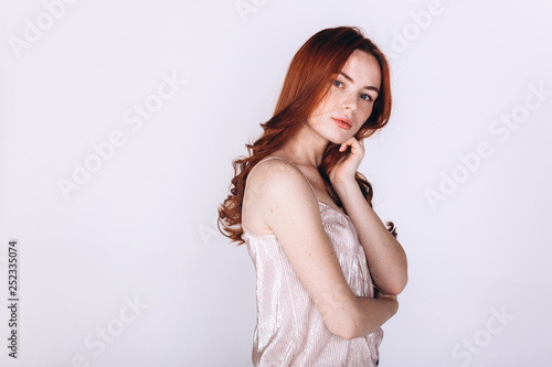 Close up portrait of young ginger pretty emotional caucasian girl with freckles posing in studio on grey background. Beauty, casual, fashion concept