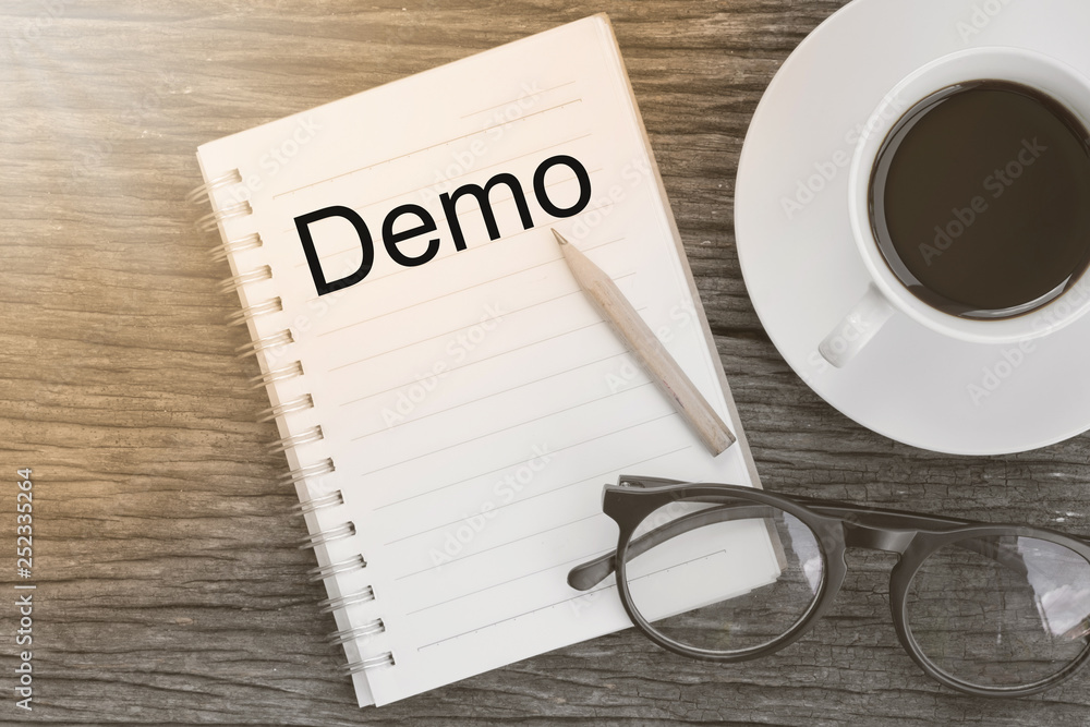 Demo word on notebook with glasses, pencil and coffee cup on wooden table. Business concept. Demo word on notebook with glasses, pencil and coffee cup on wooden table. Business concept.