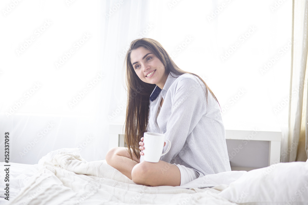 Young beautiful happy brunette woman in black silk dressing gown lying in bed, drinking morning coffee, white cup. Womens day holiday Young beautiful happy brunette woman in black silk dressing gown lying in bed, drinking morning coffee, white cup. Womens day holiday