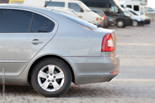 Side view of silver car parked in paved parking lot area on blurred suburb road background on bright sunny day. Transportation and parking concept