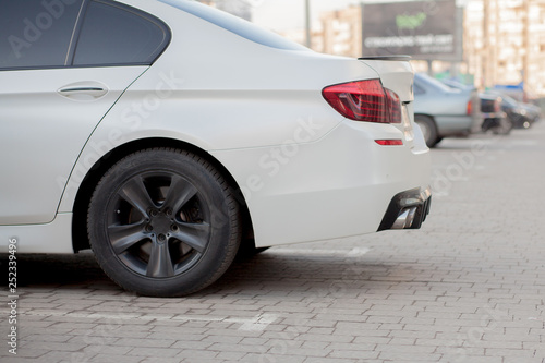 Side view of white car parked in paved parking lot area on blurred suburb road background on bright sunny day. Transportation and parking concept